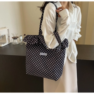 Detail of black polka dot canvas tote bag with ruffle trim and logo patch on shoulder