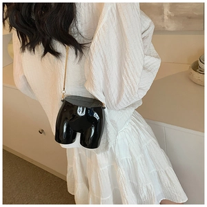 Creative black body-shaped crossbody bag with gold chain strap on white dress