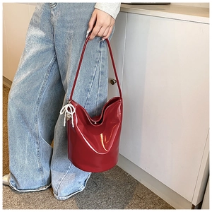 Detail of red patent leather bucket bag with white pearl bow charm and shoulder strap