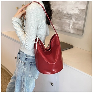 Detail of red patent leather bucket bag with pearl bow and heart charm on a model