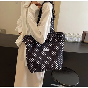Detail view of black polka dot canvas tote bag with ruffle trim and logo patch