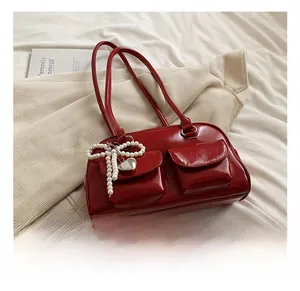 Detail of red shiny PU shoulder bag with pearl bow accents and heart pendant charm