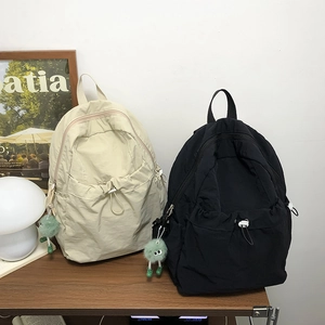 Zaini minimalisti in nylon beige e nero con un simpatico ciondolo a forma di mostro verde