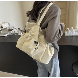 Detail einer cremefarbenen Kordelzug-Tasche mit plissierter Nylon-Textur und schwarzem Verschluss
