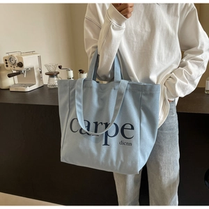 Detail view of light blue canvas tote bag with carpe text in a minimalist coffee shop setting