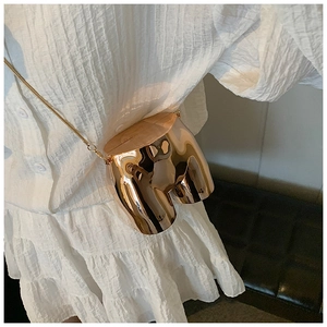 Close-up of artistic gold torso-shaped crossbody bag with polished mirror finish metal
