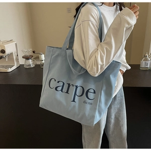 Detail of light blue canvas tote bag with carpe dicnn text shown on a shoulder