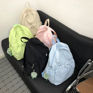 Vista dettagliata di zaini in nylon nei colori beige, verde, rosa, nero e blu con ciondoli morbidi