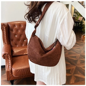 Brown corduroy crescent crossbody bag shown on model in a cozy indoor setting