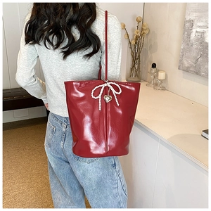 Detail of burgundy glossy PU shoulder bag featuring pearl bow and metal heart charm