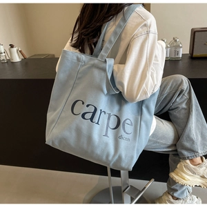 Detail of light blue canvas tote bag with carpe dicnn print carried over the shoulder