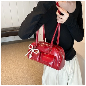 Detail view of red faux leather handbag featuring front pockets and pearl bow charm