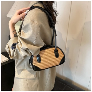 Close-up of the woven straw underarm bag with black leather trim worn on the shoulder