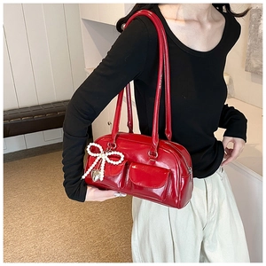 Detail view of red glossy patent leather shoulder bag with pearl bow and heart charm