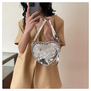 Detail of a silver sequin heart-shaped crossbody bag shown on a model suit