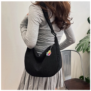 Detail view of the black corduroy half-moon crossbody bag with colorful bear charm pendant