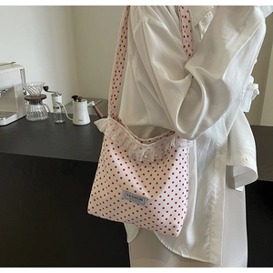 Close-up of polka dot crossbody bag with lace ruffles, pearls, and a logo label