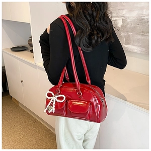 Detail of red patent leather shoulder bag featuring pearl bow and heart metal charm