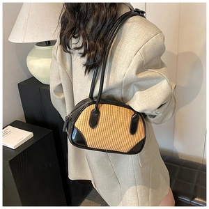 Detail view of woven straw shoulder bag with black PU leather trim on a modern prop background