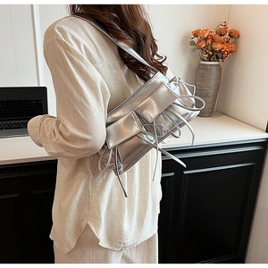 Silver metallic pleated shoulder bag with tie detail shown on a model in a stylish setting