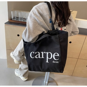 Detail of black canvas tote bag with white carpe text worn over the shoulder in a room