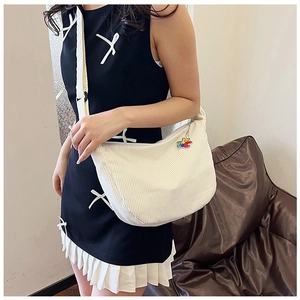 Detailed view of white corduroy hobo bag with a cute bear charm worn with a black dress