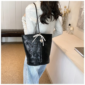 Detail of glossy black PU bucket bag with pearl bow and silver heart pendant