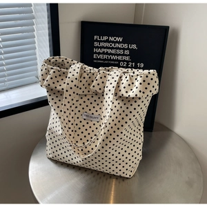 Polka dot canvas tote bag with ruffle trim design and white brand label on silver table