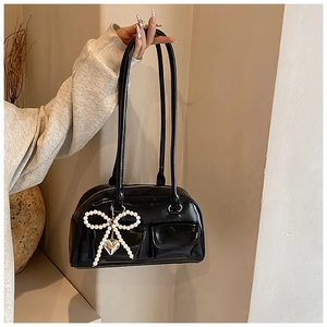 Detail of black glossy PU shoulder bag featuring dual front pockets and pearl bow charm