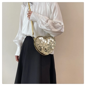 Detailed close-up of heart-shaped crossbody bag with glittering golden sequins and leather strap