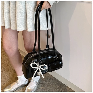 Close-up of black patent leather bag with a pearl bow charm and silver heart pendant detail
