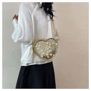 Detail of a heart-shaped crossbody bag with golden sequins and leather shoulder strap