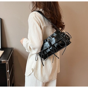 Detail of trendy black PU leather shoulder bag with stylish pleated design on a model