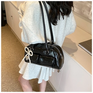 Detail of black patent leather handbag featuring pearl bow charm and heart pendant
