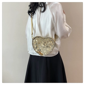 Detail view of heart-shaped crossbody bag with golden sequins on a model in minimalist setting