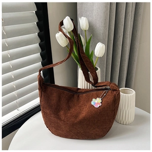 Dark brown corduroy half-moon crossbody bag with cute bear pendant on a white table