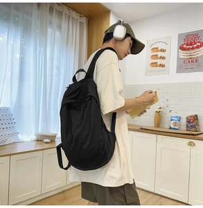 Detail of spacious black nylon backpack with side straps worn by model in casual style
