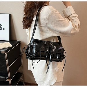 Detail of a black glossy PU leather shoulder bag featuring multi-pocket workwear design