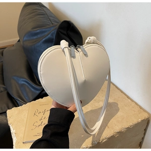 Dettaglio della borsa a tracolla color crema a forma di cuore con cerniere in argento