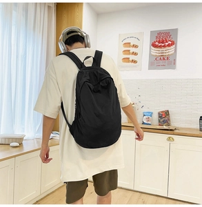 Close-up view of a minimalist black nylon backpack worn by a man in a modern casual setting