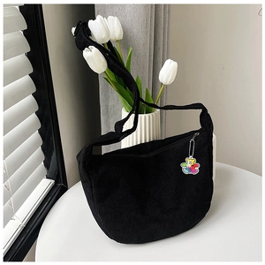 Minimalist black corduroy crescent crossbody bag with a cute bear charm on white table