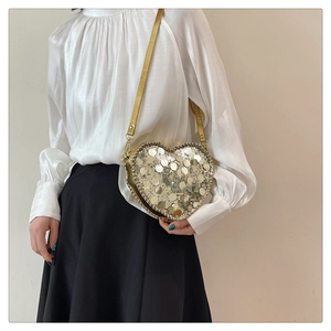 Detail of a heart-shaped golden sequin crossbody bag with a delicate metal chain strap