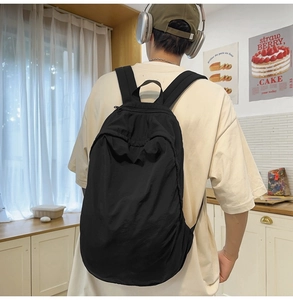 Side view of a minimalist black nylon backpack on a model in a bright interior setting