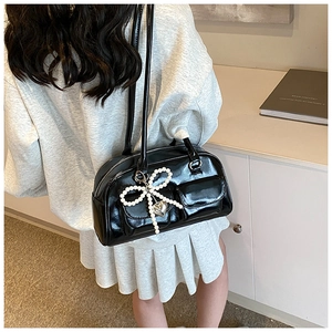 Detail of black patent leather shoulder bag with pearl bow charm and silver heart pendant