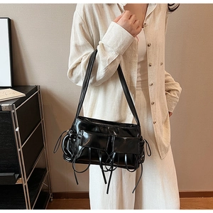 Detailed close-up of glossy black faux leather shoulder bag featuring stylish side straps