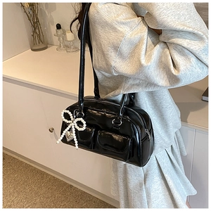 Close-up of black patent leather handbag with pearl bow heart charm and dual front pockets