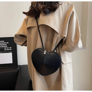Vista dettagliata di una borsa a tracolla nera a forma di cuore con un trench coat kaki