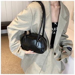 Detail of a black glossy PU leather shoulder bag with sleek long handles on a model
