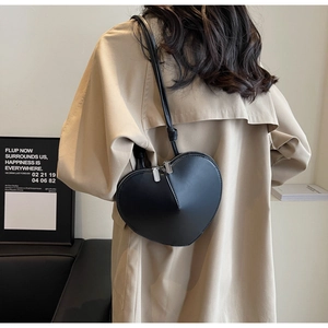 Dettaglio di una borsa a tracolla nera a forma di cuore indossata su un trench beige