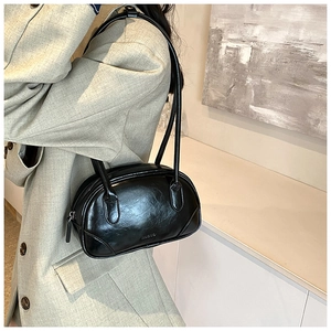 Close-up of a black glossy PU leather shoulder bag with embossed logo on gray blazer